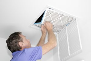 Mature man taking out a dirty air filter from a home ceiling air return vent. Male removing a dirty air filter with both hands in a house from a HVAC ceiling air vent.