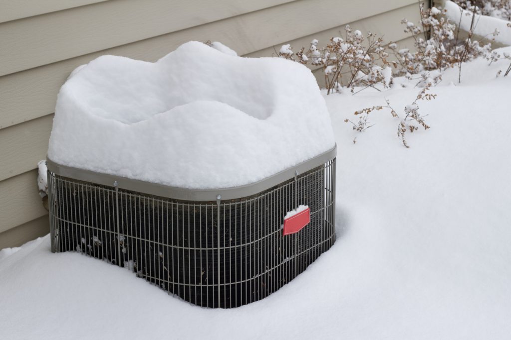 View of an exterior air conditioner unit covered with deep snow following a snow storm