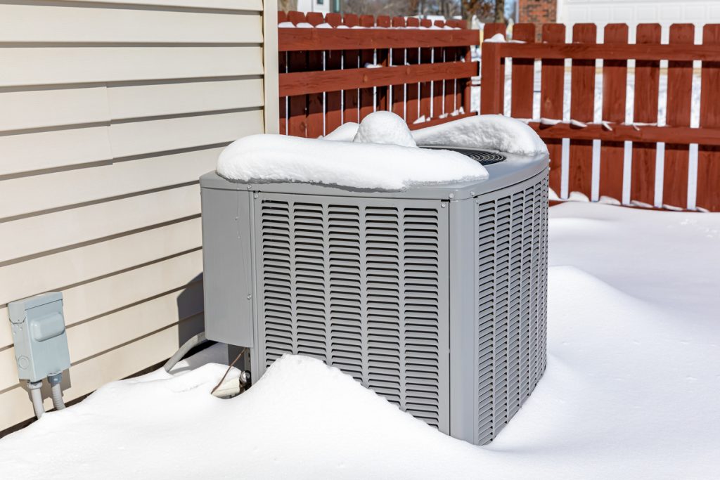 House air conditioning unit covered in snow during winter.. Concept of home air conditioning, hvac, repair, service, winterize and maintenance.